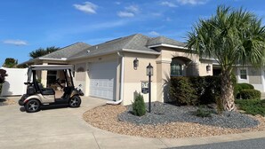 A residential house with a garage, a golf cart, and a palm tree. - Cozy Collier Retreat with Fire Pit, Dog Friendly Near Brownwood (The Villages)