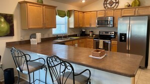 A kitchen with wooden cabinets, a stainless steel refrigerator, a microwave, and a large island with chairs. - Cozy Collier Retreat with Fire Pit, Dog Friendly Near Brownwood (The Villages)