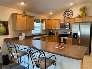 A kitchen with wooden cabinets, a stainless steel refrigerator, a microwave, and a large island with chairs. - Cozy Collier Retreat with Fire Pit, Dog Friendly Near Brownwood (The Villages)