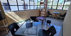 Ein Zimmer mit Glastisch, schwarzen StĂŒhlen, Schreibtisch aus Holz und BĂŒcherregal.