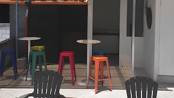 Un área de estar al aire libre con sillas y mesas, un toldo amarillo y un edificio al fondo.