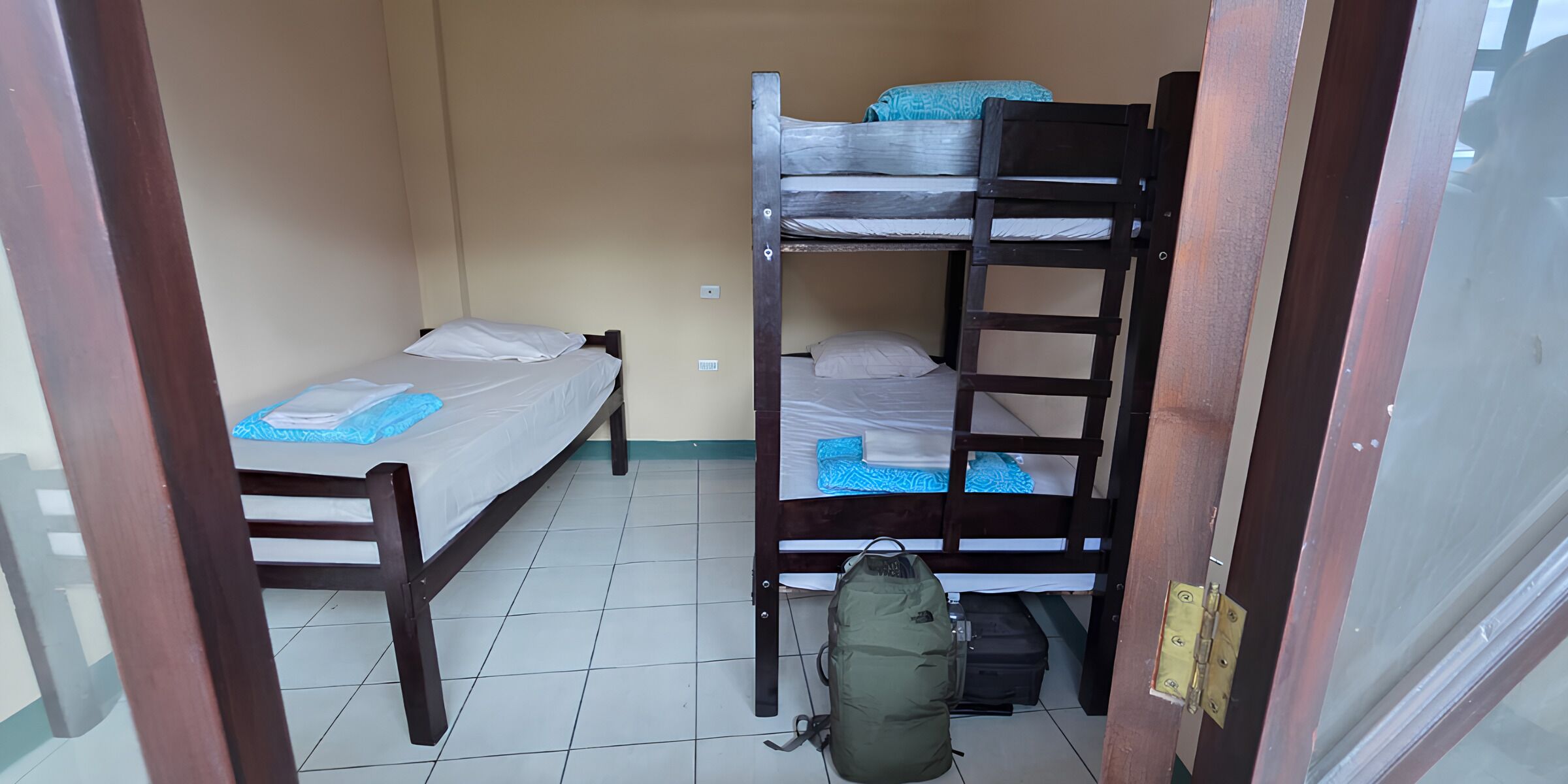 Un alojamiento pequeño, de una sola habitación, con una cama litera, una cama individual y una silla de madera.