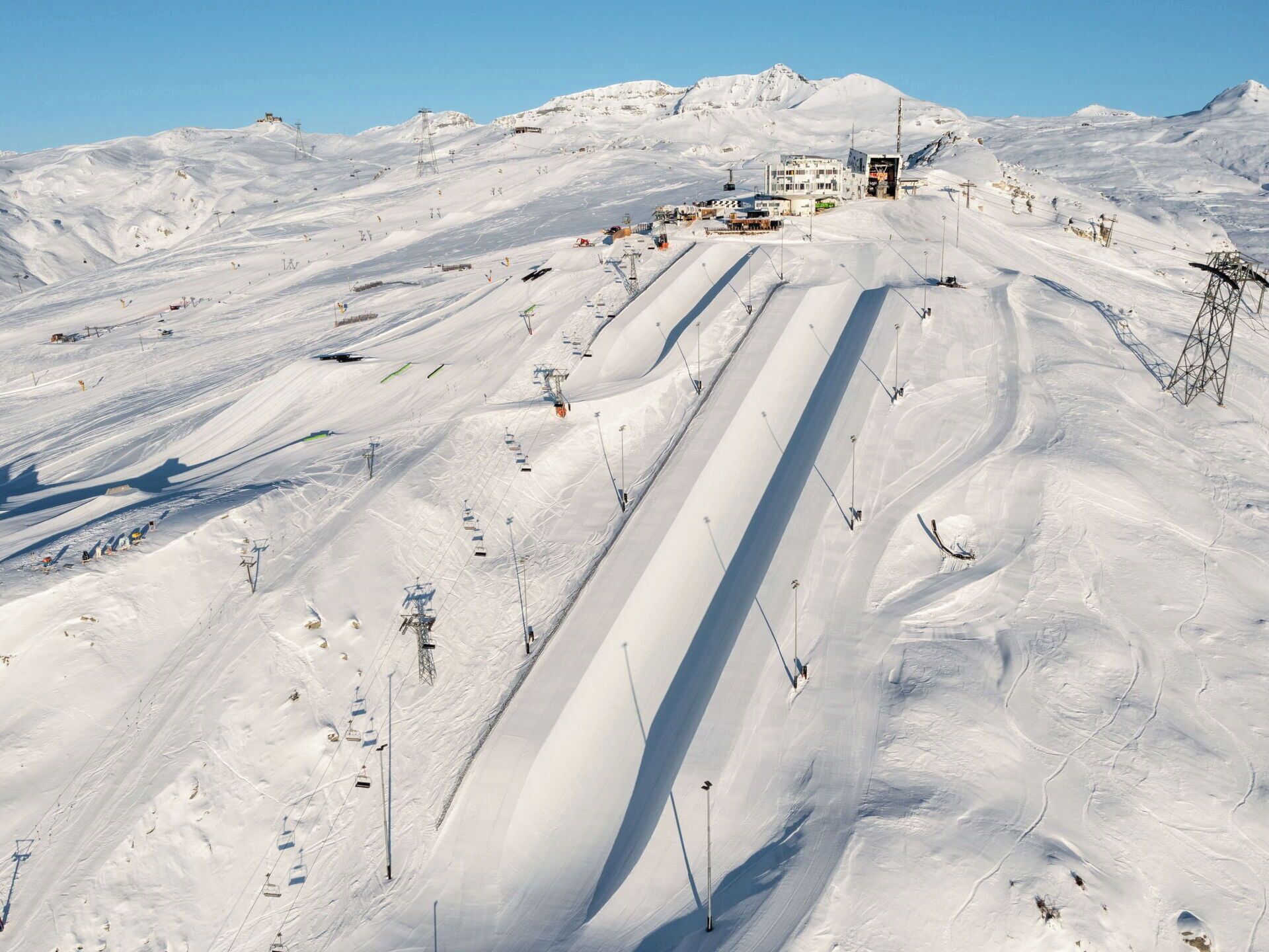 Une piste de ski enneigée, avec des remontées mécaniques et un bâtiment situé au sommet.
