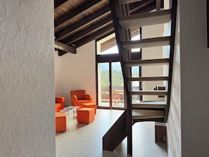 Ein modernes Interieur mit einer Holztreppe, orangefarbenen Sitzgelegenheiten und großen Fenstern mit Blick ins Freie.