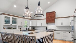 A modern kitchen with white cabinets, a central island with chairs, and pendant lighting. - Lakecation on Smith Lake – Private boat launch! Private Dock! (Crane Hill)