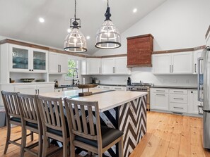 A modern kitchen with white cabinets, a central island with chairs, and pendant lighting. - Lakecation on Smith Lake – Where Vacation Memories Begin! (Crane Hill)