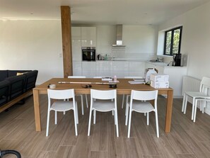 Eine moderne Küche mit weißen Schränken, einem Holztisch mit vier Stühlen und einem schwarzen Sofa im Wohnbereich.