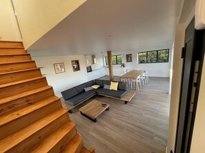 Ein moderner Wohnbereich mit Treppe, einem Ecksofa, einem Esstisch mit Stühlen und einer Küche im Hintergrund.