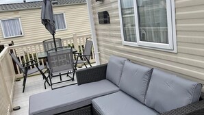 Un espacio al aire libre techado con sofá y sillones, una mesa y una parrilla.