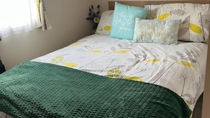 Una cama con colcha de estampado floral, una manta verde y dos almohadas con texto.