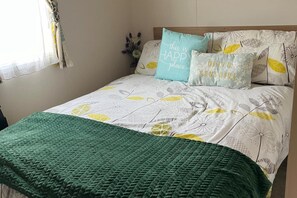 A bed with a floral-patterned bedspread, a green throw blanket, and two pillows with text. - Sunny Nook Cozy Cabin Retreat Selsey, Gated Garden (Chichester)