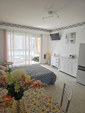 Un dormitorio con cama, escritorio, silla, televisor y una zona de cocina.