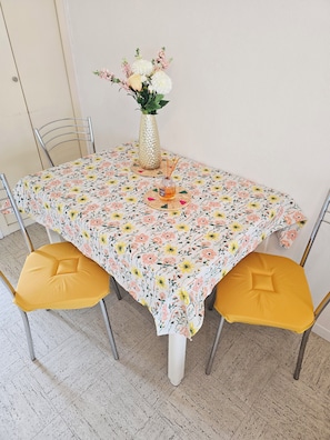 Una mesa de comedor con mantel floral, un florero con flores y dos sillas amarillas acolchadas.