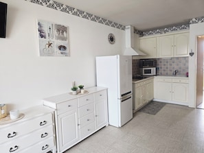 Una cocina con armarios blancos, un refrigerador, un microondas y un lavamanos. Hay un adorno de pared y una planta pequeña en la encimera.