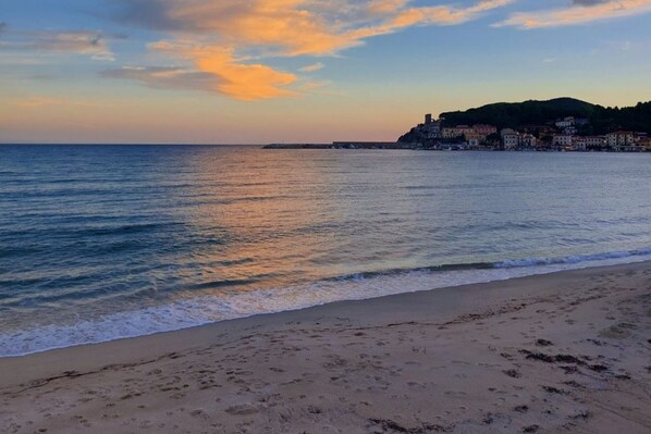 A beach with a calm sea, a sandy shore, and buildings in the background. - Losanna Apartment (La Pila)