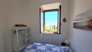 Um quarto com cama, janela com vista, guarda-roupa e luminária fixada na parede.
