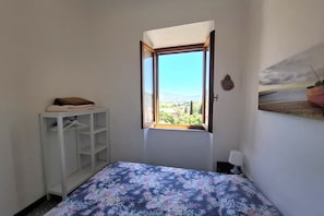 Ein Schlafzimmer mit Bett, Fenster mit Blick, Kleiderschrank und Wandlampe.