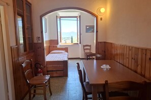 A room with a wooden dining table, two chairs, a bed, a window with a view, and a door leading to another room. - Losanna Apartment (La Pila)