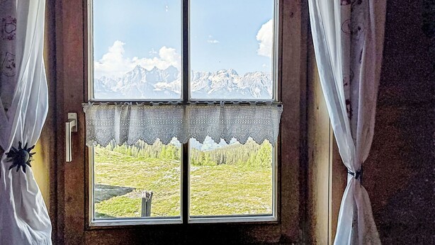 Una finestra con vista sulle montagne, tende e un fermaglio.