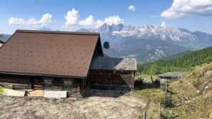 Un rustico rifugio di montagna con tetto spiovente, un'antenna parabolica e vista sulle montagne innevate.