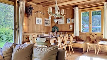 Ein Holzinnenraum mit einem für sechs Personen gedeckten Esstisch, einer Couch und einer Chandelier.