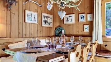 Ein Holzinterieur mit einem für sechs Personen gedeckten Esstisch, gerahmten Bildern an der Wand und einer Chandelier.