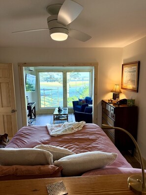 Ein Schlafzimmer mit Bett, Schreibtisch, Stuhl, Lampe und Blick ins Freie.