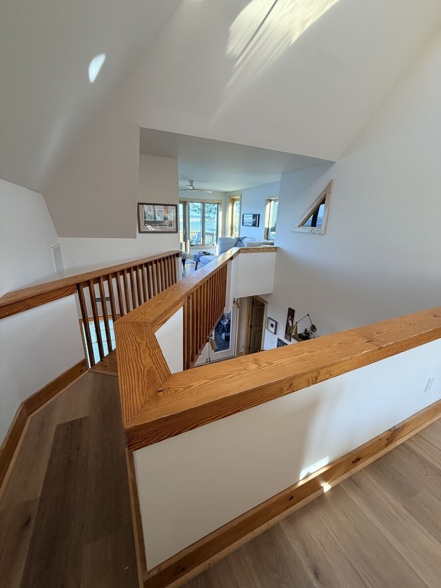 Een modern interieur met een houten trap, witte muren en uitzicht op een zithoek.