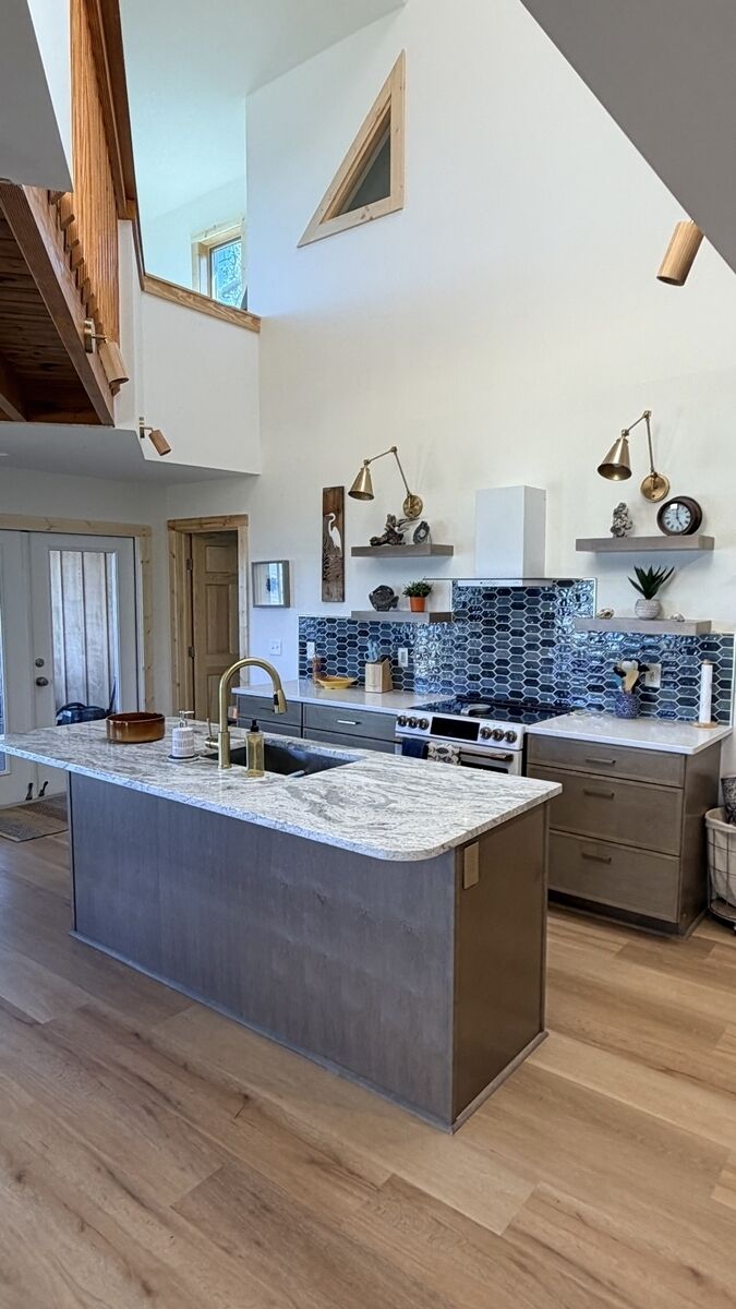 Una cocina moderna con una isla central, piso de madera y techo alto con vigas a la vista.