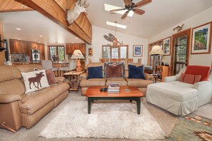 A spacious living room with leather sofas, a wooden ceiling fan, and a fireplace.