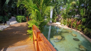 Un pontile in legno conduce a una piscina cristallina circondata da vegetazione lussureggiante.