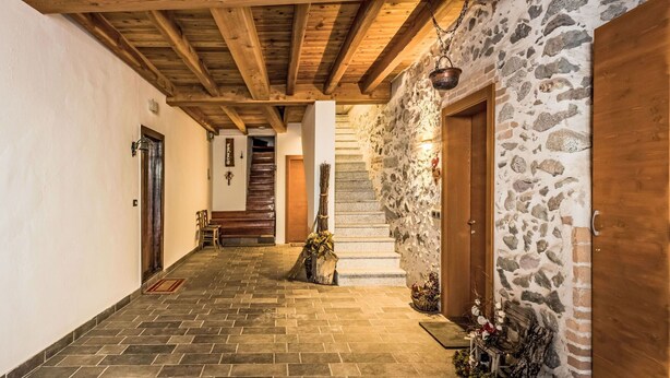 Un couloir aux murs de pierre, avec un escalier en bois, un banc et une porte rustique.