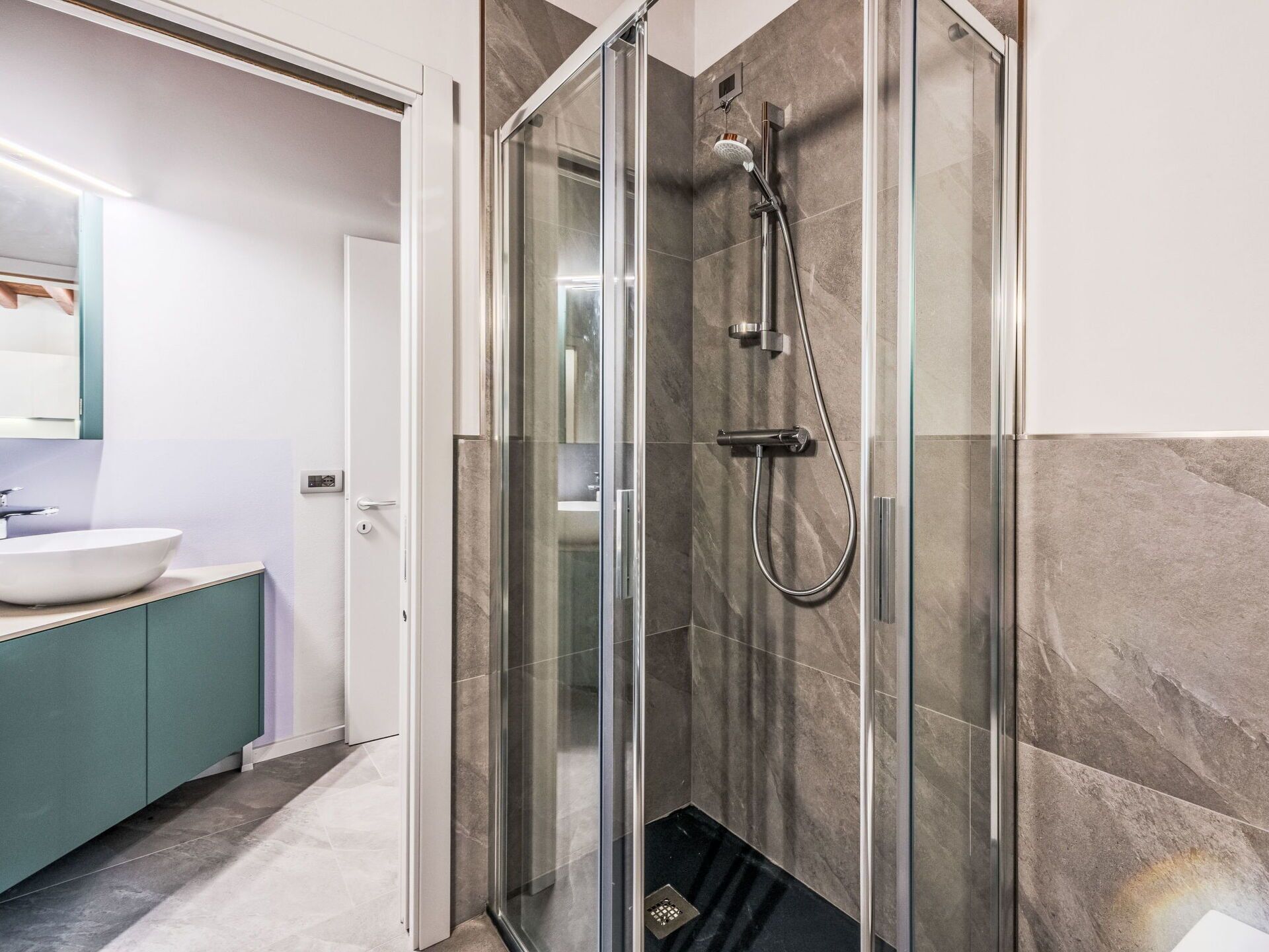Un baño moderno con ducha de vidrio, lavamanos blanco y tocador color turquesa.