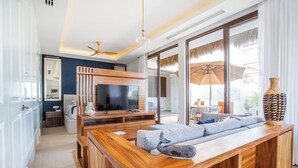 A modern living room with a wooden entertainment unit, a flat-screen TV, a sofa, and a large window with a view. - Elegance - Jungle meet with private pool (heated) (La Cruz de Huanacaxtle)