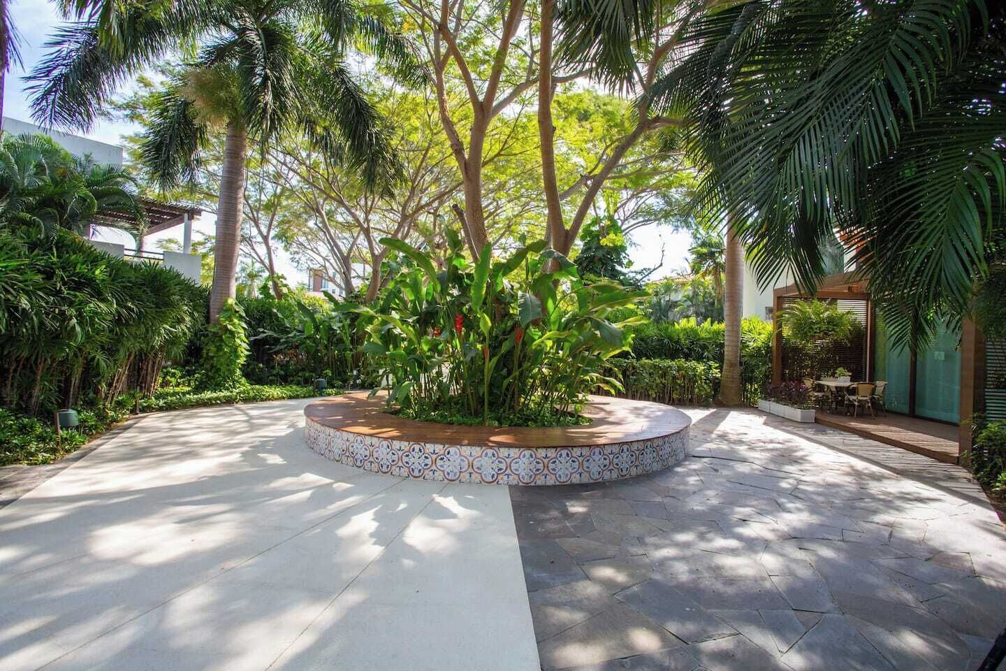 A circular garden with a tiled border, surrounded by various tropical plants and trees.