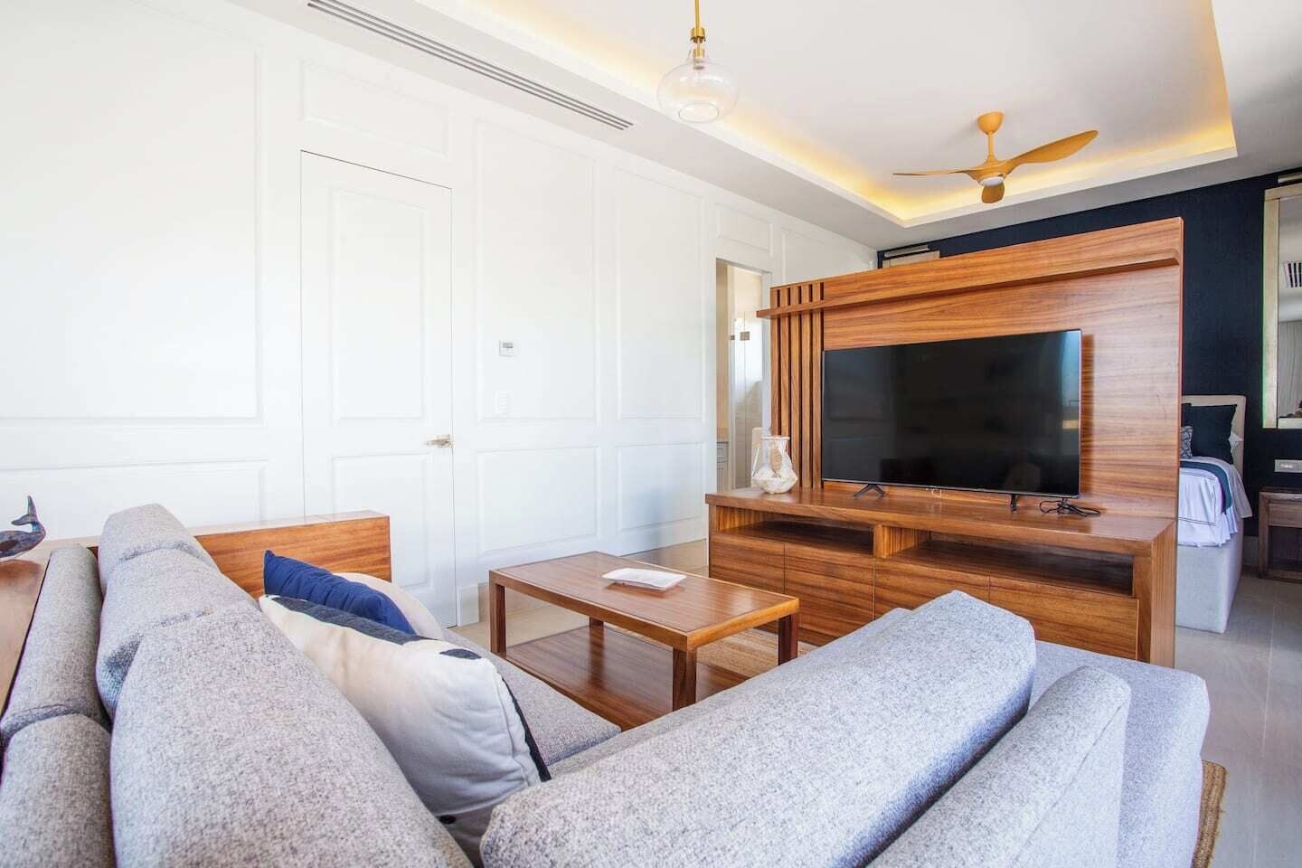 A modern living room with a sofa, TV, wooden entertainment unit, and ceiling fan.