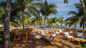 A wooden deck with outdoor seating, palm trees, and a view of the beach. - Elegance - Jungle meet with private pool (heated) (La Cruz de Huanacaxtle)