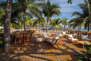 A wooden deck with outdoor seating, palm trees, and a view of the beach. - Elegance - Jungle meet with private pool (heated) (La Cruz de Huanacaxtle)