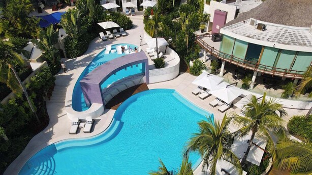 A large pool with sun loungers and umbrellas, surrounded by palm trees and a building with a curved roof. - Elegance - Jungle meet with private pool (heated) (La Cruz de Huanacaxtle)