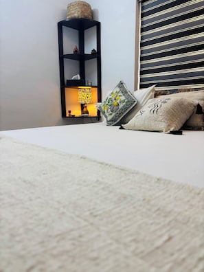 A neatly made bed with a white bedspread, a decorative pillow with a floral pattern, and a bedside table with a lamp and a small decorative item. - Villa Lemon Garden (Varkala)