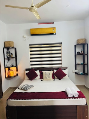Une chambre d’hôtel équipée d’un lit, d’un ventilateur de plafond, d’un climatiseur mural et d’objets décoratifs disposés sur des étagères.