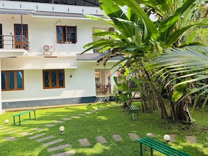 A two-story building with a balcony, a garden with a bench, and a large banana plant. - Villa Lemon Garden (Varkala)
