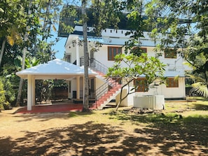 A two-story building with a covered outdoor seating area, a staircase, and a small tree. - Villa Lemon Garden (Varkala)