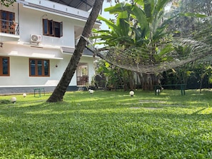 A white building with a balcony, a palm tree, and a well-maintained lawn. - Villa Lemon Garden (Varkala)