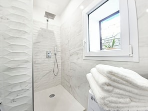 Une salle de bain moderne avec une douche, une fenĂȘtre donnant sur un beau paysage et une pile dâserviettes.