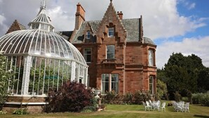 A large, historic building with a prominent glass conservatory and a well-maintained garden with outdoor seating. - Kingsknowes Hotel (Galashiels)