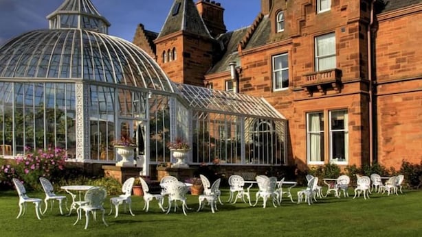 A large glass conservatory with a dome roof, surrounded by white metal chairs and tables, set against a brick building with a steeply pitched roof. - Kingsknowes Hotel (Galashiels)