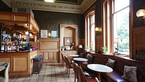 A bar area with stools, a bar counter, and a seating area with a bench and round tables. - Kingsknowes Hotel (Galashiels)