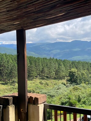 Une vue depuis un porche abritĂ©, donnant sur un paysage boisĂ© avec des montagnes Ă lâhorizon.