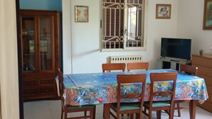 Zona pranzo con tavolo ricoperto da una tovaglia colorata, circondato da sedie di legno.